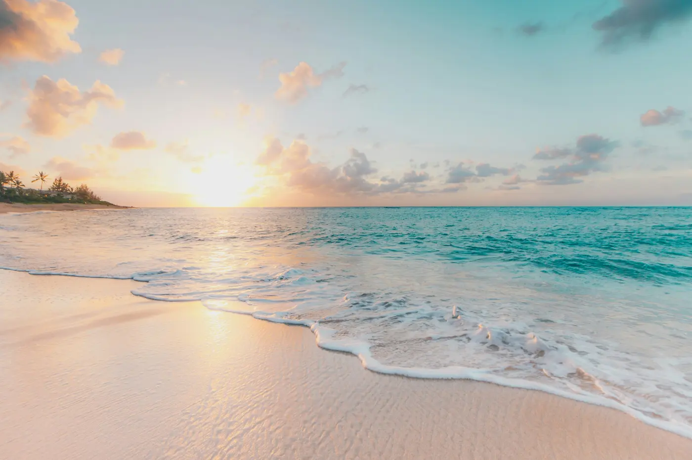 Low sun over an empty sandy beach, with small waves washing up the shore.