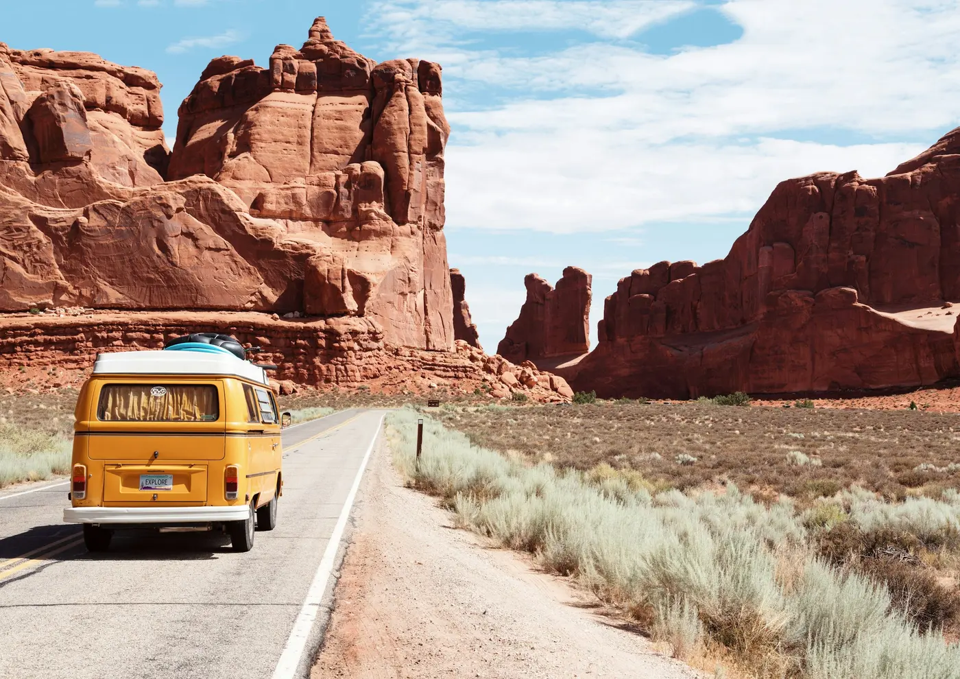 A yellow van on a desert highway, with red rock formations beyond the road near Moab, Utah.