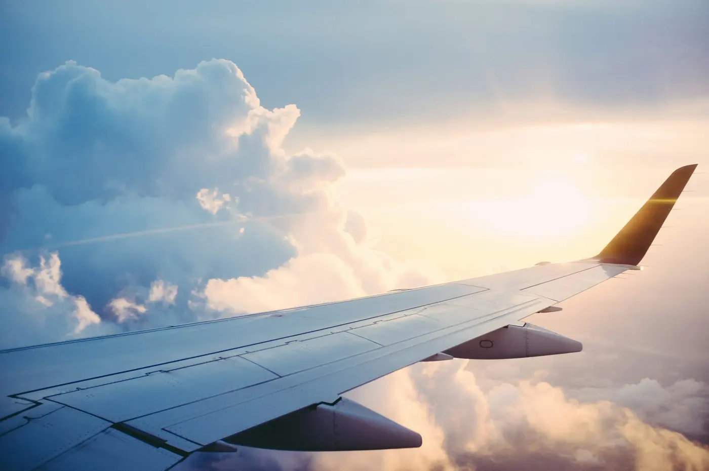 An airplane wing above a layer of clouds, with warm light along the horizon.